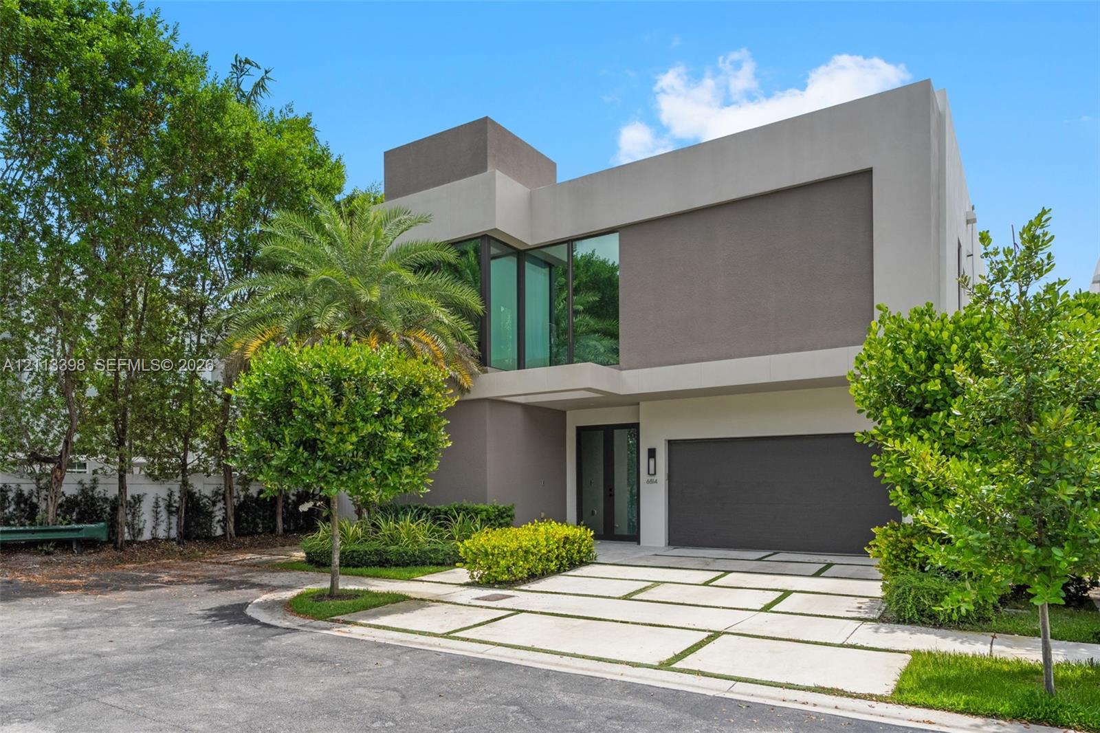 Modern multi-level exterior featuring smooth stucco facade, floor-to-ceiling glass windows, integrated covered entryway, and segmented concrete paver driveway with turf accents