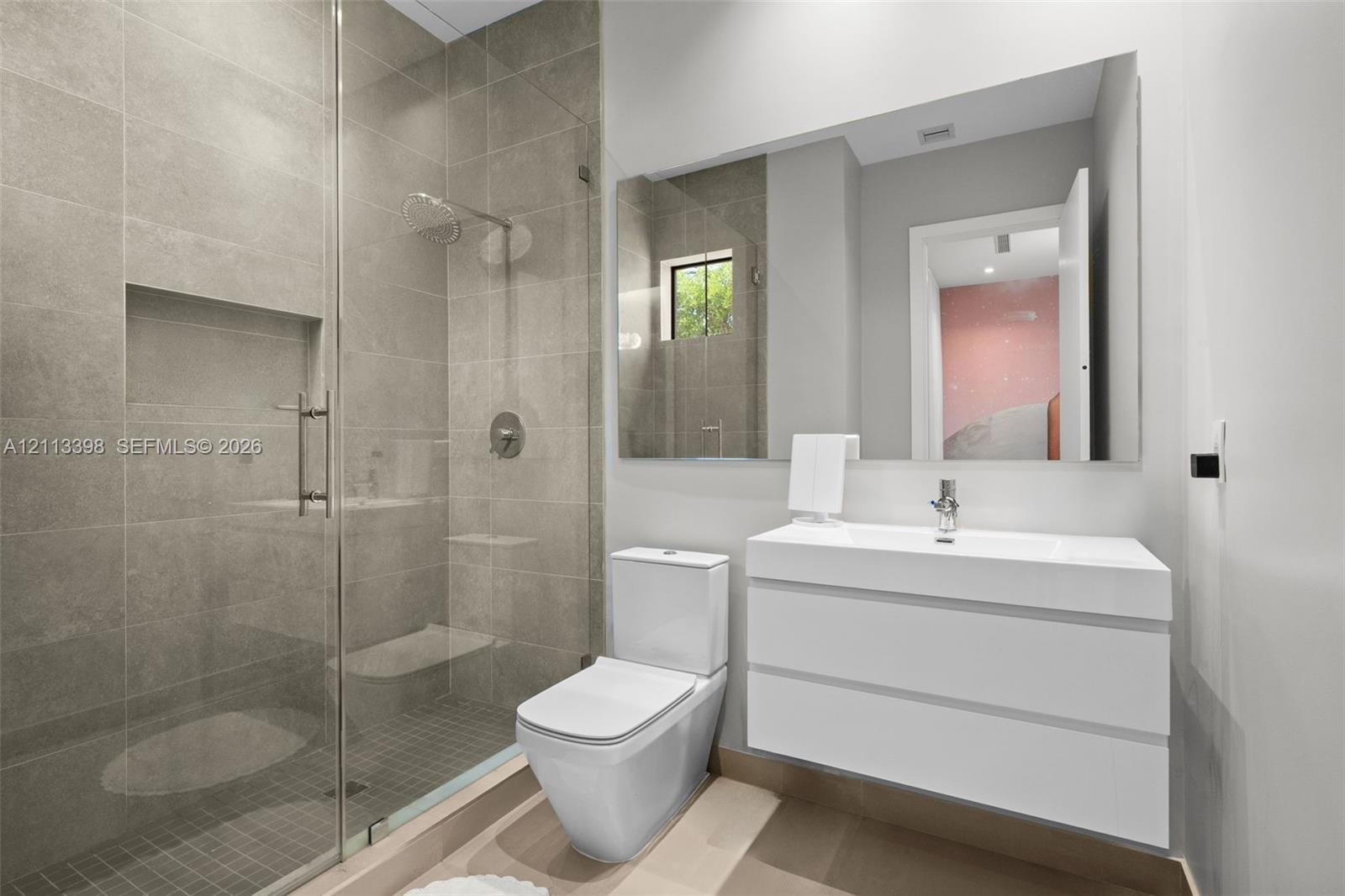 Modern bathroom featuring a glass-enclosed shower with tiled walls and a built-in recessed niche, a white floating vanity with a seamless integrated sink, and a wall-to-wall mirror