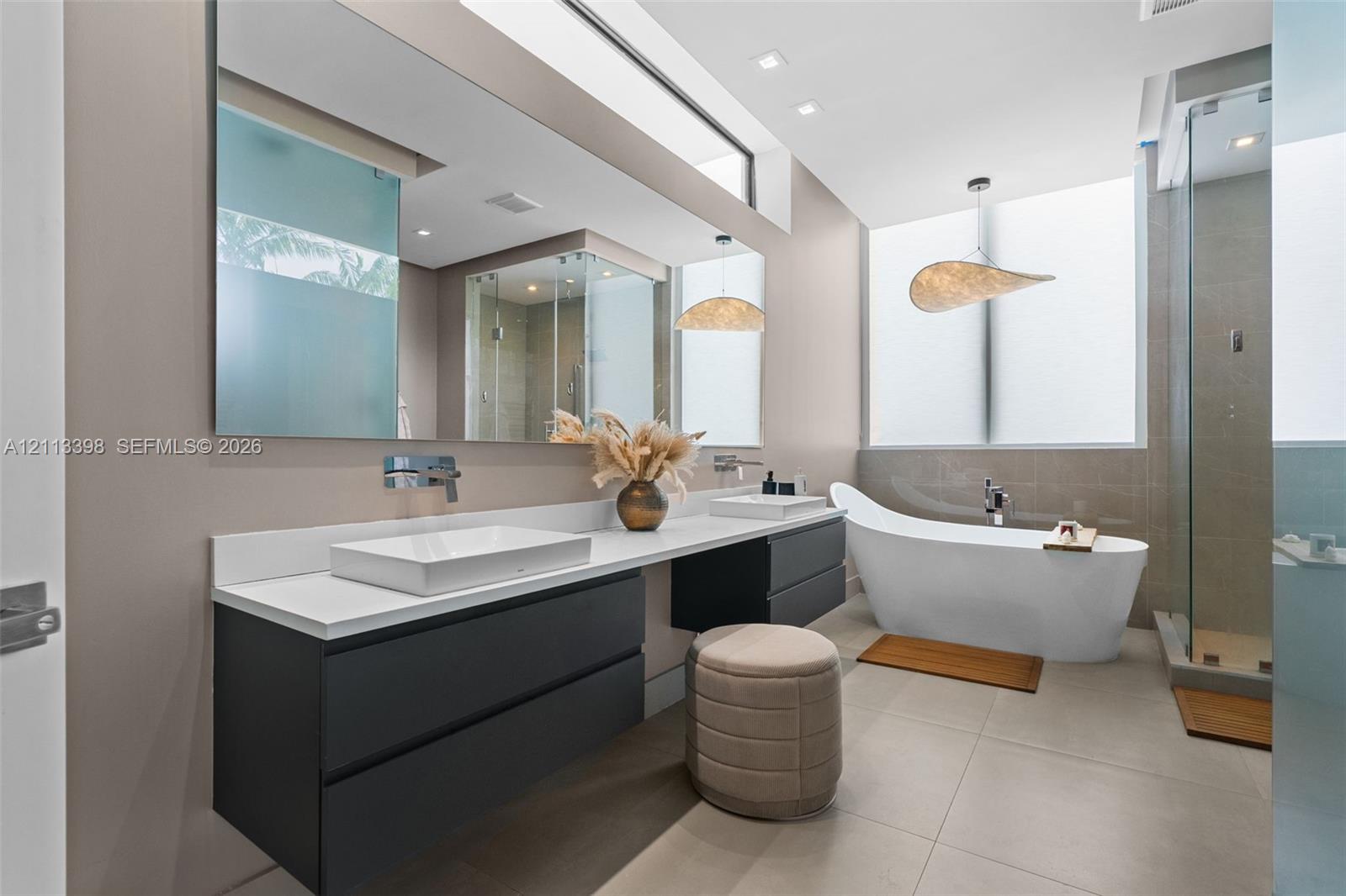 Floating dual-vanity with rectangular vessel sinks, quartz countertop, wall-mounted faucets, freestanding soaking tub, and glass-enclosed shower with large-format tile flooring