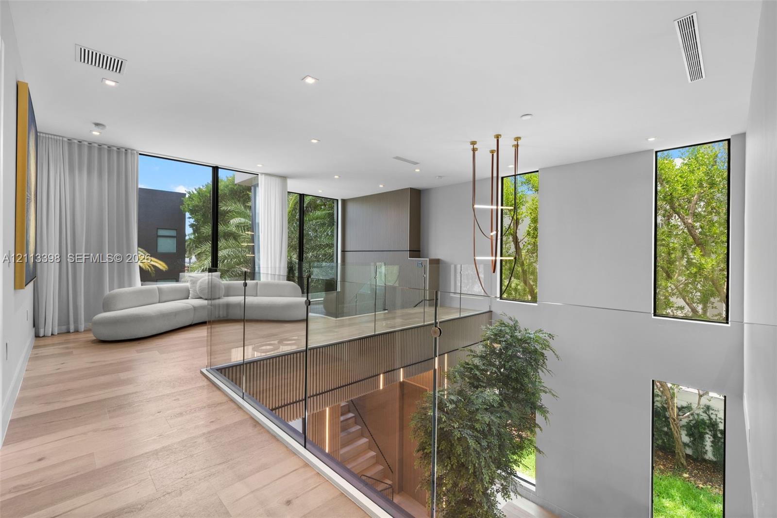 Open-concept floor plan featuring wood-finish flooring, floor-to-ceiling windows, a glass panel railing, and integrated linear lighting