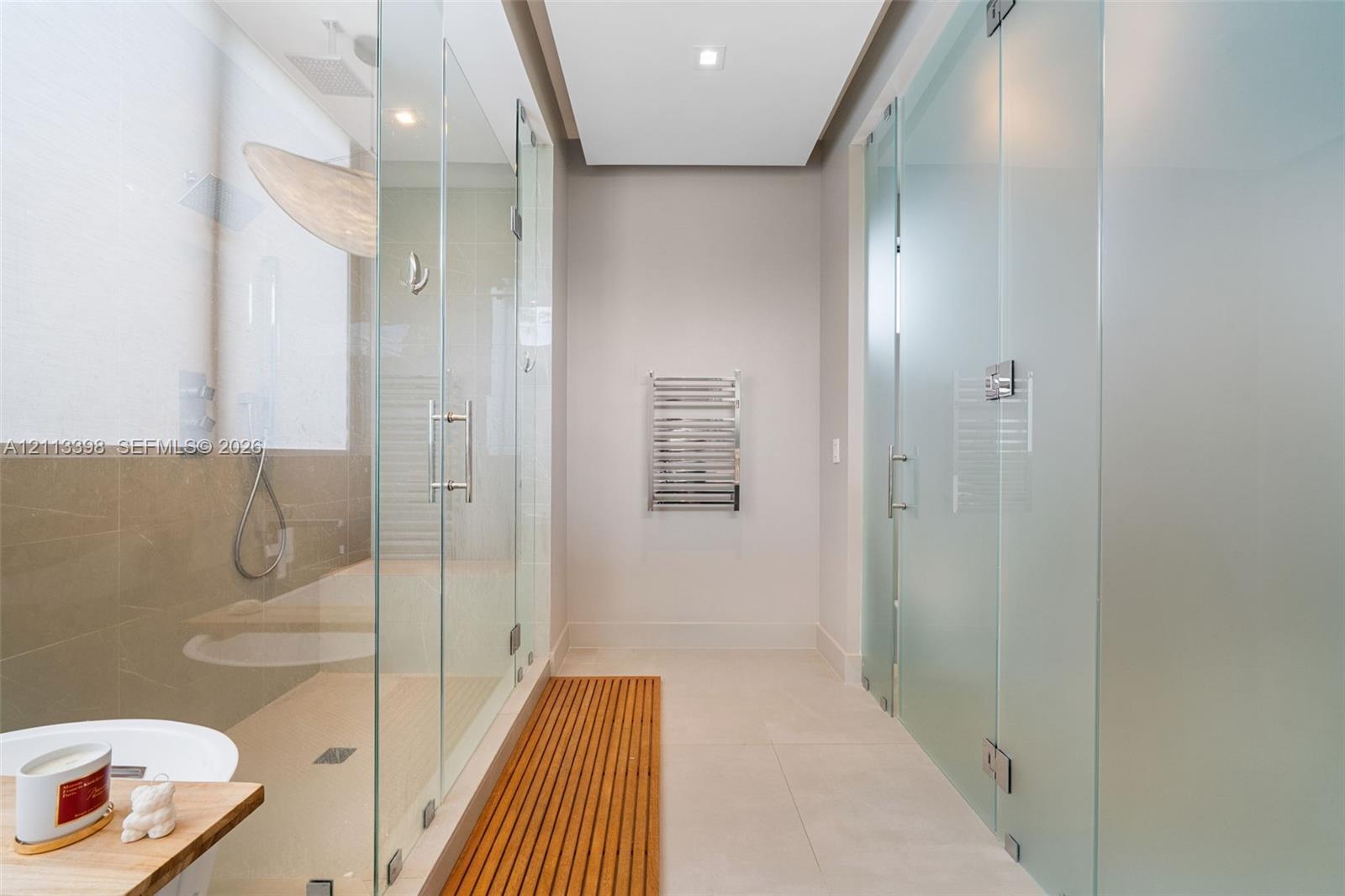 Walk-in shower featuring a glass enclosure, floor-to-ceiling frosted glass partitioning, recessed ceiling lighting, wall-mounted heated towel rack, and a slatted wood floor inlay
