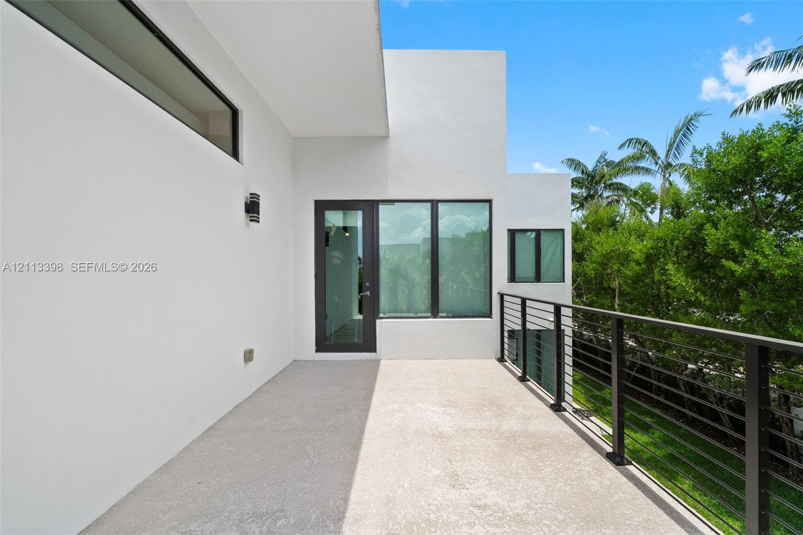 Covered exterior terrace featuring a smooth concrete floor, minimalist white stucco exterior walls, dark-framed expansive windows, and a metal horizontal-bar railing