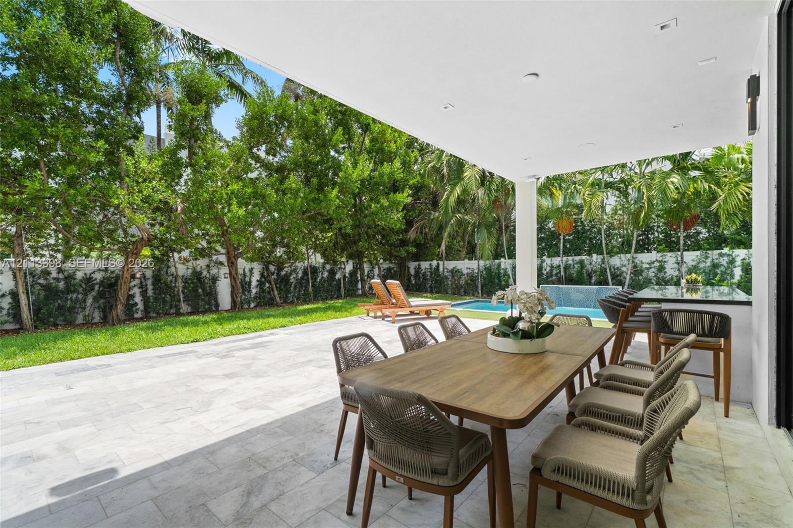 Covered outdoor patio featuring large-format stone tiling, integrated recessed lighting, a built-in outdoor bar with countertop, an in-ground swimming pool, and a manicured lawn