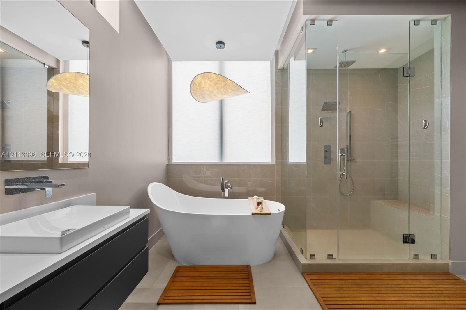 Modern floating vanity with a vessel sink and wall-mounted faucet, freestanding soaking tub, glass-enclosed walk-in shower with a built-in bench, and large-format tile flooring
