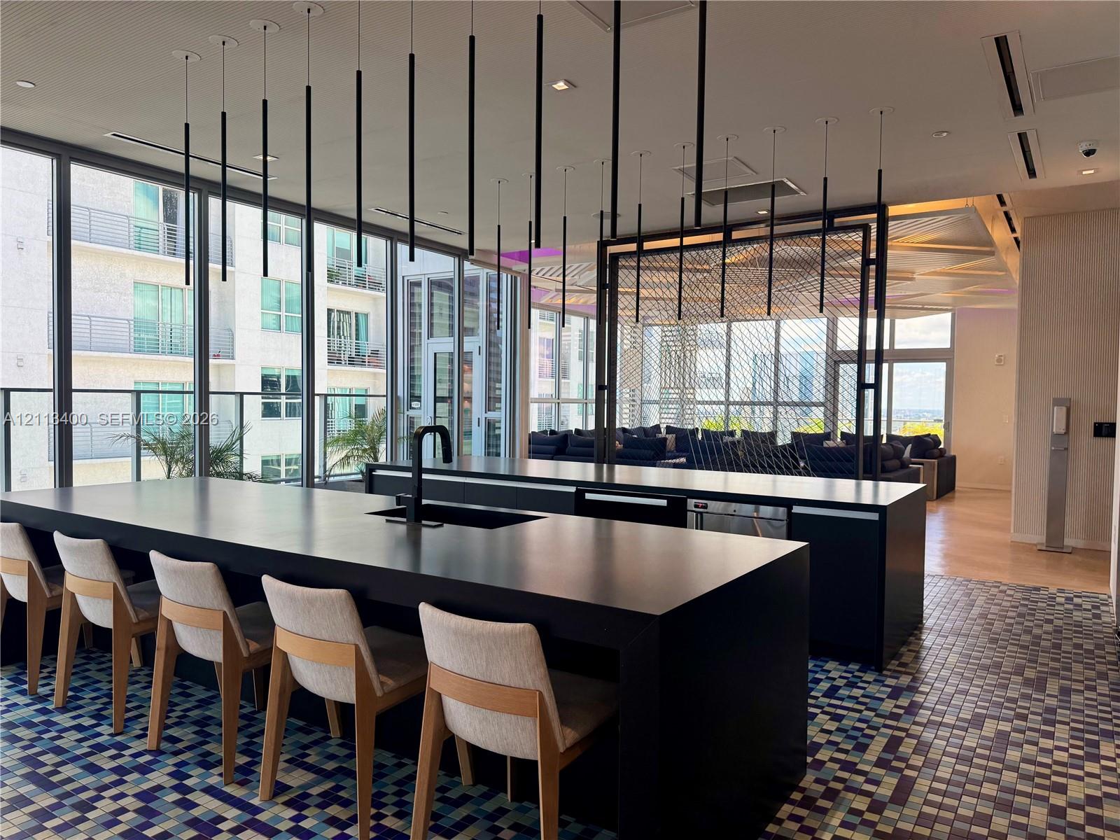 Expansive kitchen island featuring a dark solid-surface countertop, integrated basin, and matte black faucet, illuminated by a series of minimalist pendant lights
