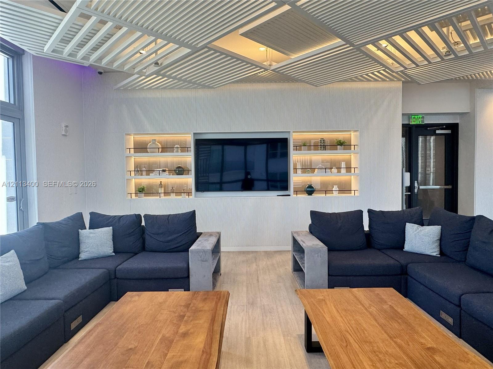 Geometric slatted ceiling design featuring recessed lighting, custom built-in wall shelving with integrated illumination, and wood-finish flooring