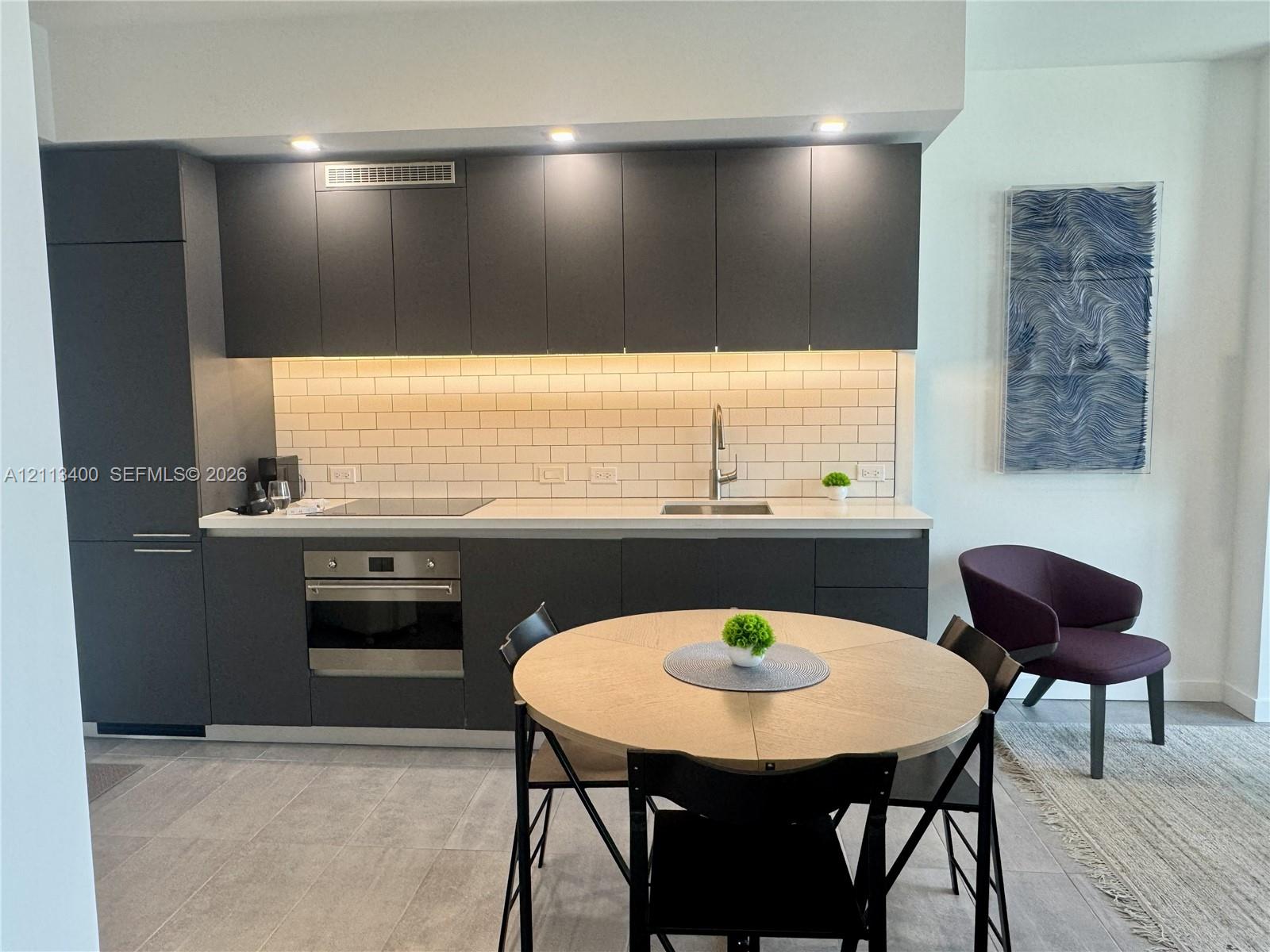 Kitchen featuring matte charcoal flat-panel cabinetry, light-toned countertop, subway tile backsplash, built-in stainless steel oven, and recessed lighting