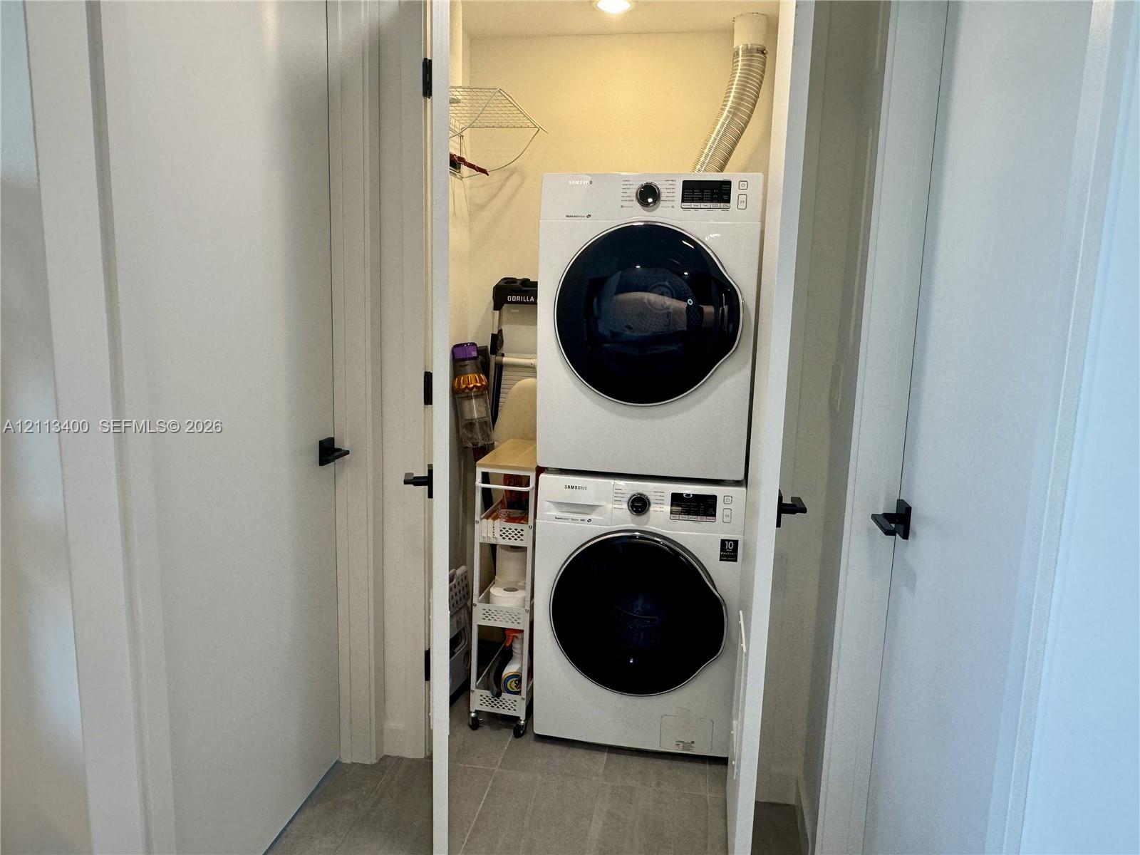 Laundry closet featuring stacked high-efficiency washer and dryer, tile flooring, and matte black door hardware
