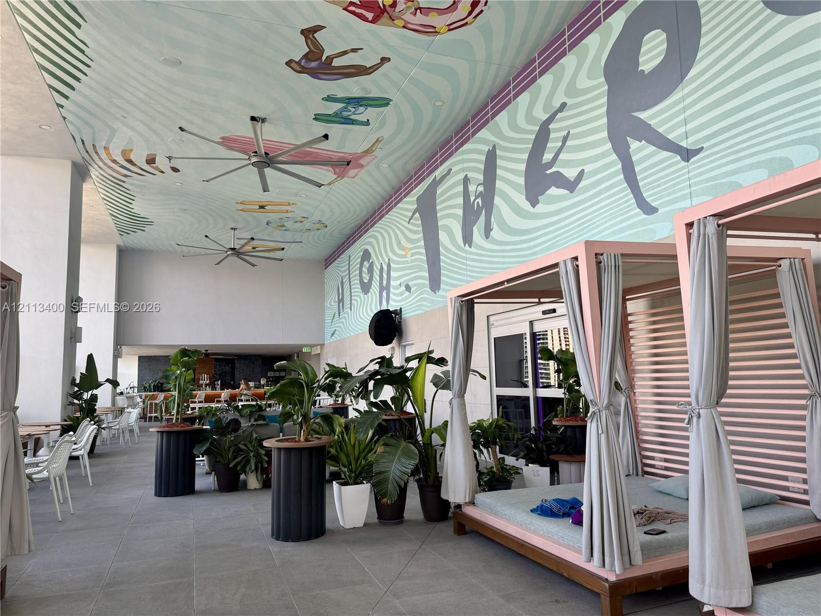 Covered outdoor lounge area featuring large-format stone flooring, ceiling-mounted industrial fans, and a decorative ceiling mural