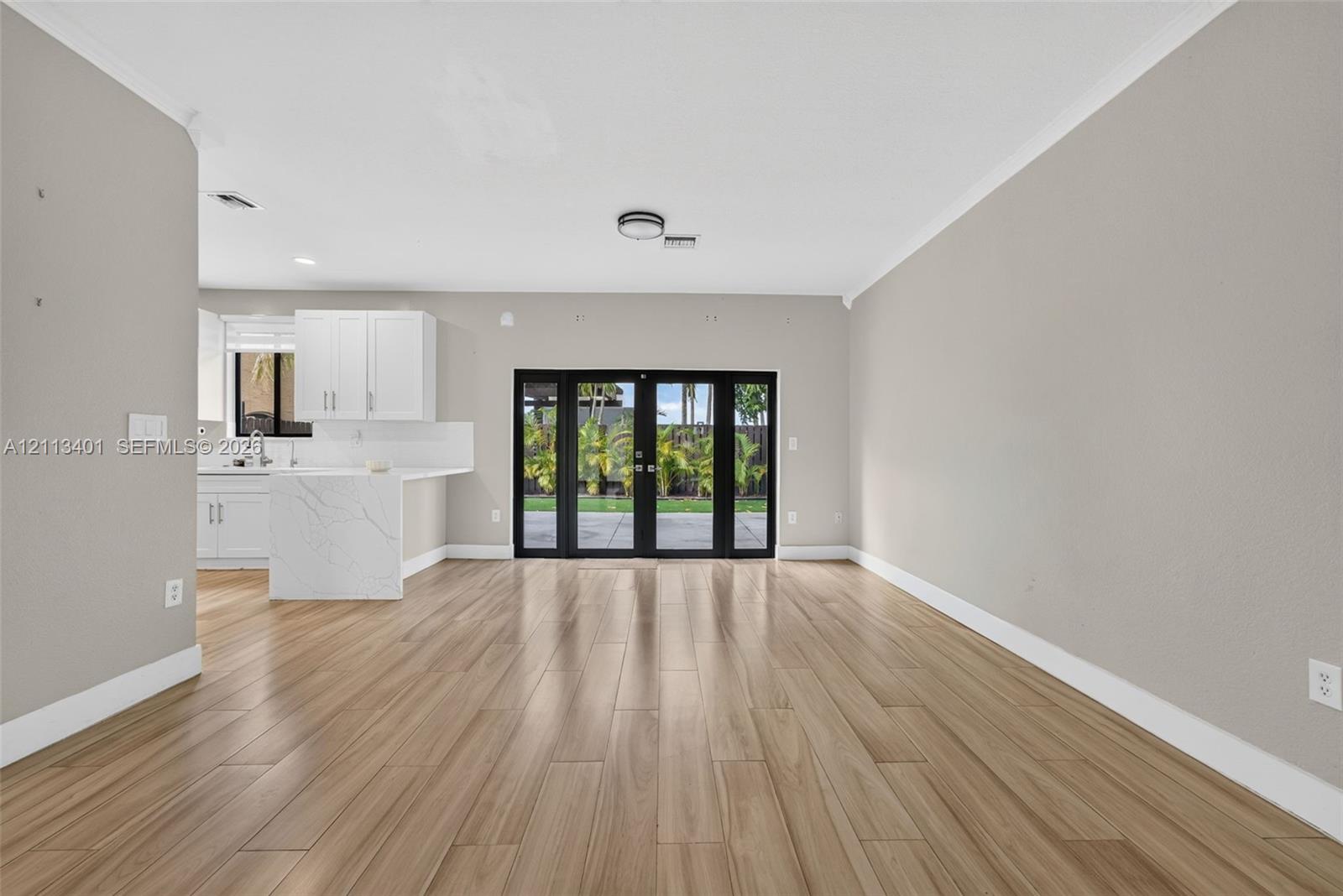 Open-concept area featuring wood-finish flooring, white cabinetry, a stone-finish waterfall-edge peninsula, and black-framed glass french doors