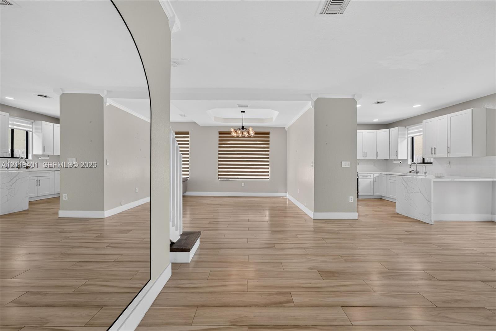 Open-concept interior featuring wood-finish tile flooring, white cabinetry with stone-finish waterfall countertops, recessed lighting, and a modern tiered tray ceiling