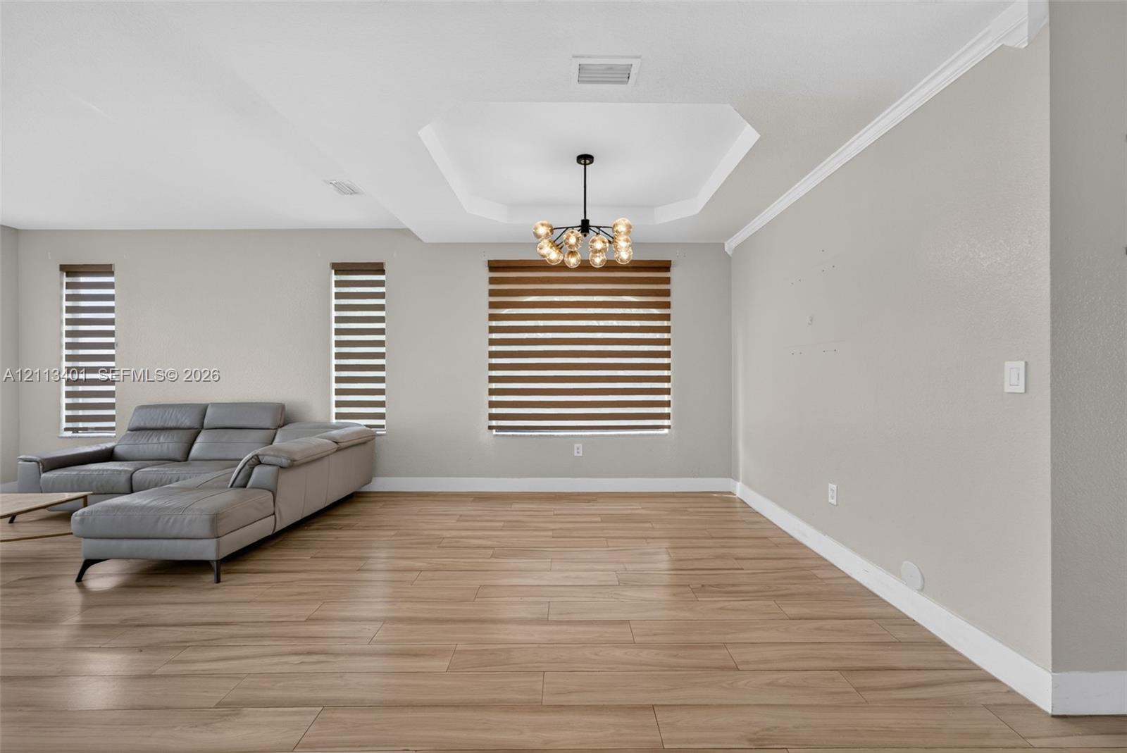 Tray ceiling, multi-light modern chandelier, wood-finish flooring, and horizontal window shades