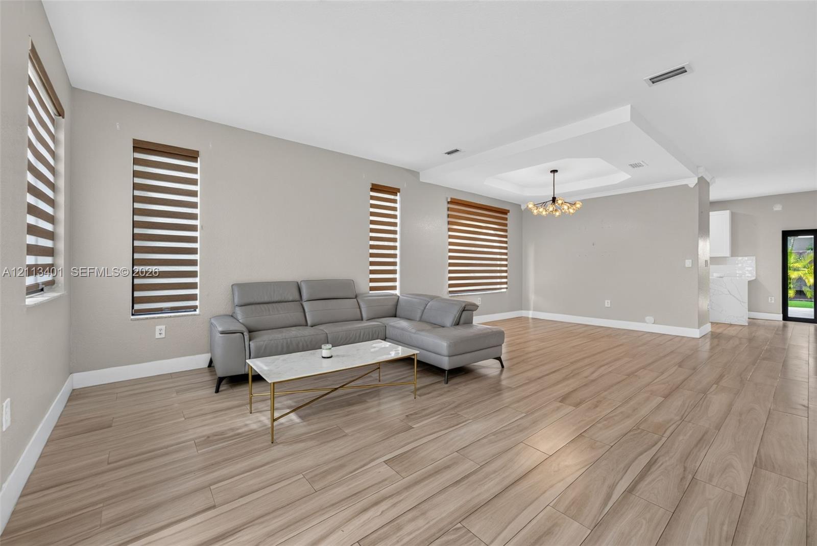 Open concept interior featuring wood-finish tile flooring, recessed tray ceiling, multi-light chandelier, and horizontal window shades