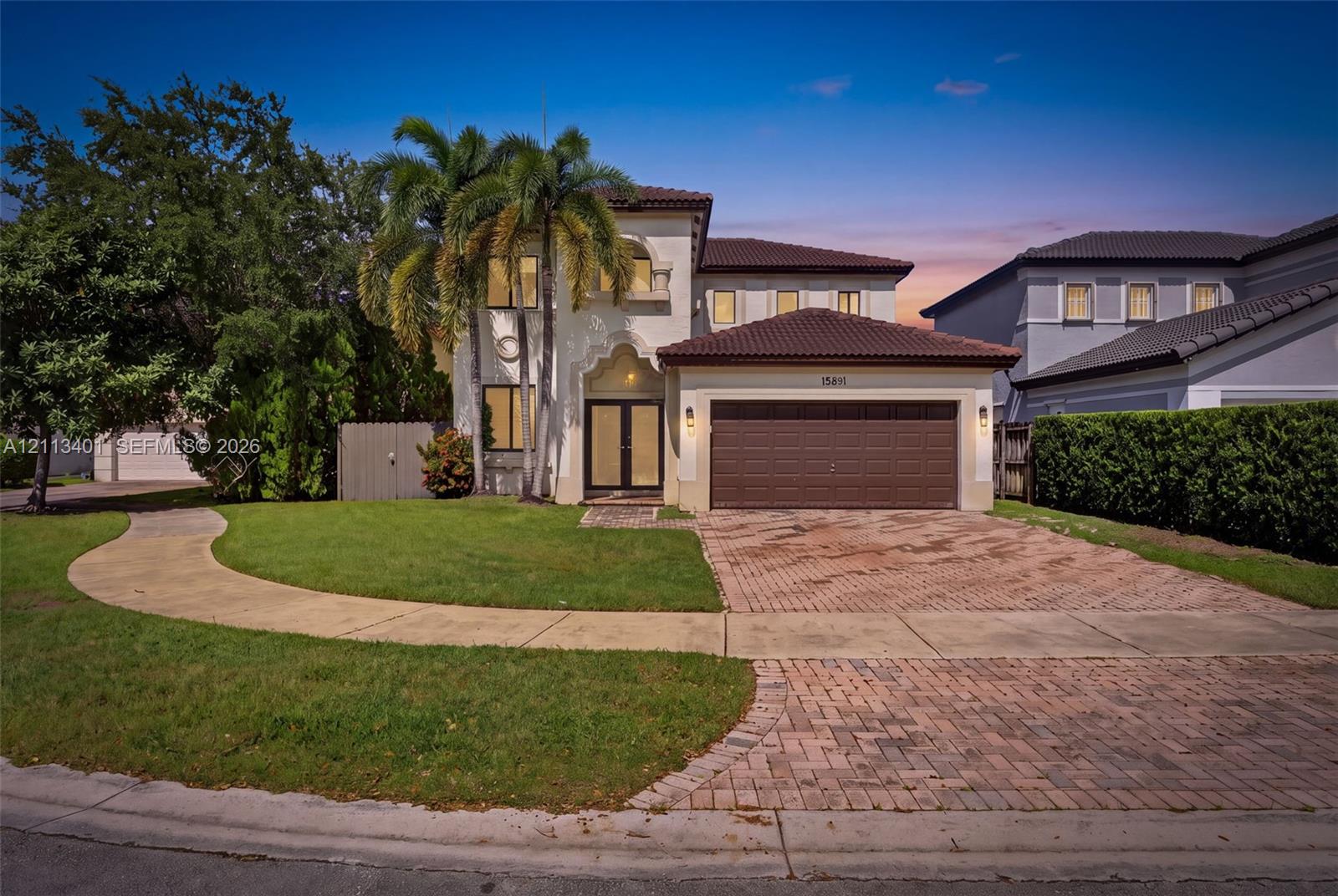 Two-story stucco exterior featuring a tiled hip roof, arched entryway, brick-paver driveway, and a two-car garage