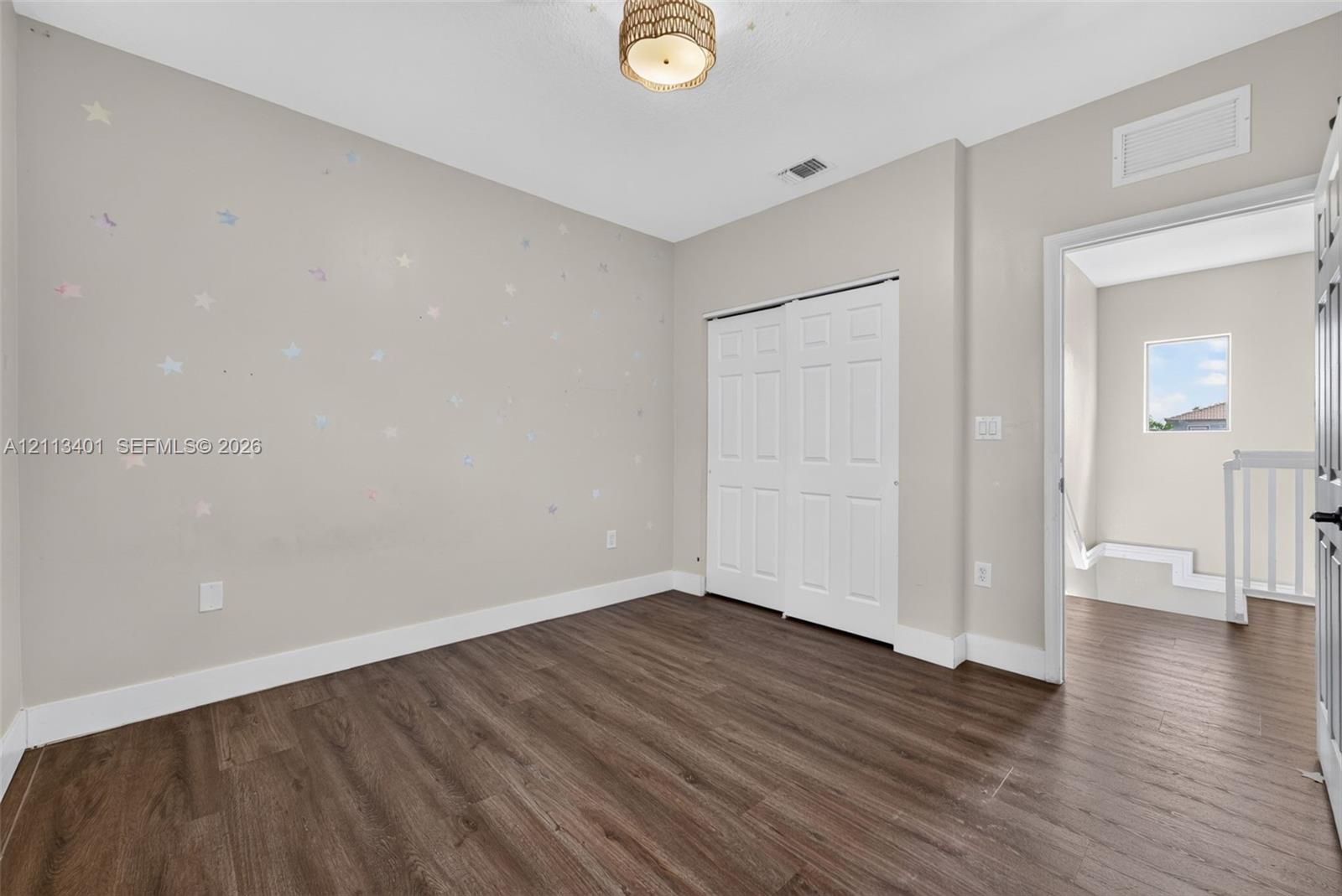 Room featuring wood-finish flooring, a double-panel sliding closet, and a neutral-toned ceiling light fixture