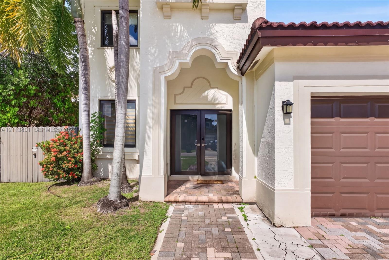 Stucco exterior featuring an arched entryway with double glass-paneled doors, a tiled roof, and a brick-paver walkway