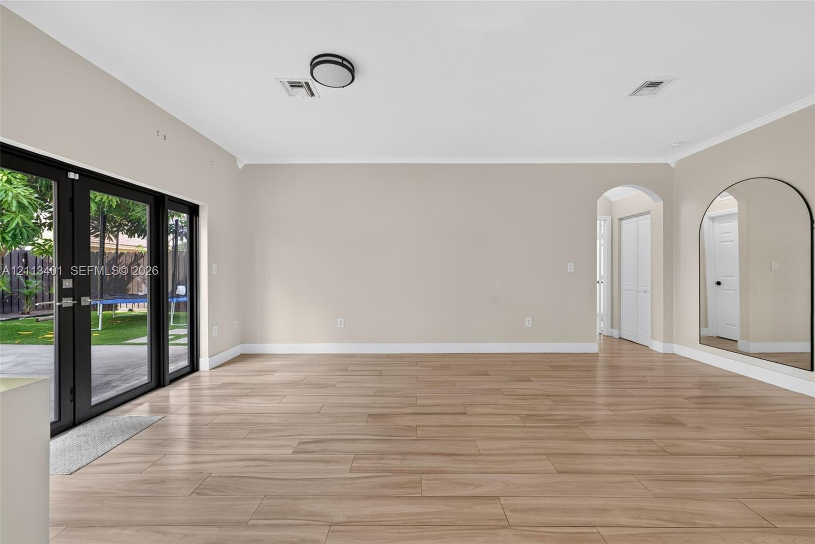 Open-concept room featuring wood-finish flooring, floor-to-ceiling glass panel double doors with black frames, a high-arched passageway, and a large arched wall-mounted mirror