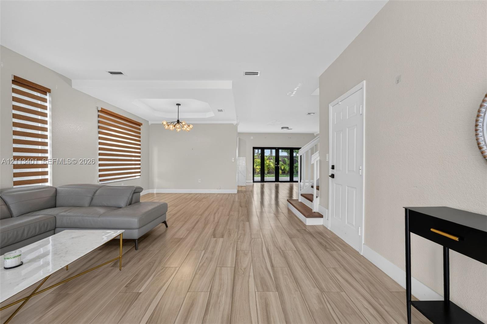 Open floor plan featuring wood-finish flooring, tray ceiling, statement chandelier, and double-paned sliding glass doors