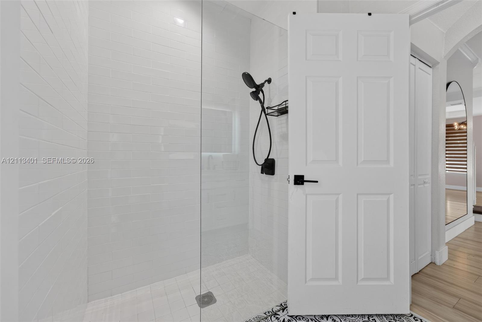 Walk-in shower with white subway tile surround, glass partition, matte black handheld shower fixture, and wood-finish flooring