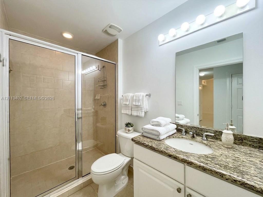 Bathroom featuring a stone-surface vanity with an integrated basin, a walk-in shower with a glass enclosure and tile surround, and a multi-bulb vanity light fixture