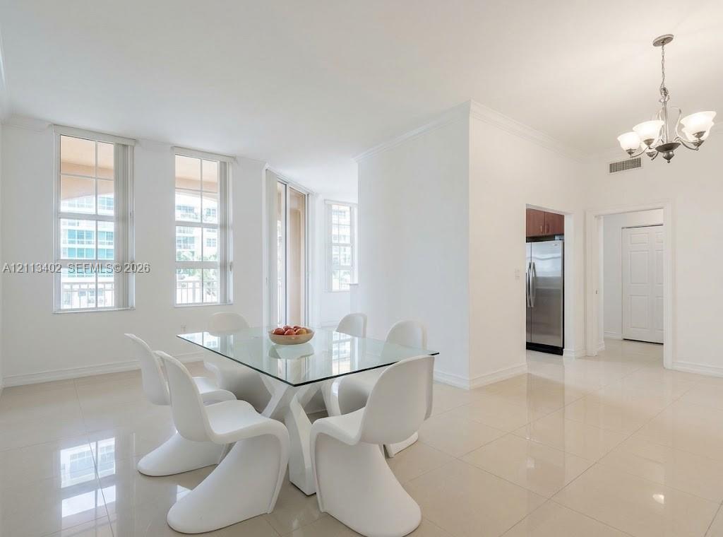 Bright open living area featuring neutral tile flooring, multi-pane windows, crown molding, and a multi-arm chandelier