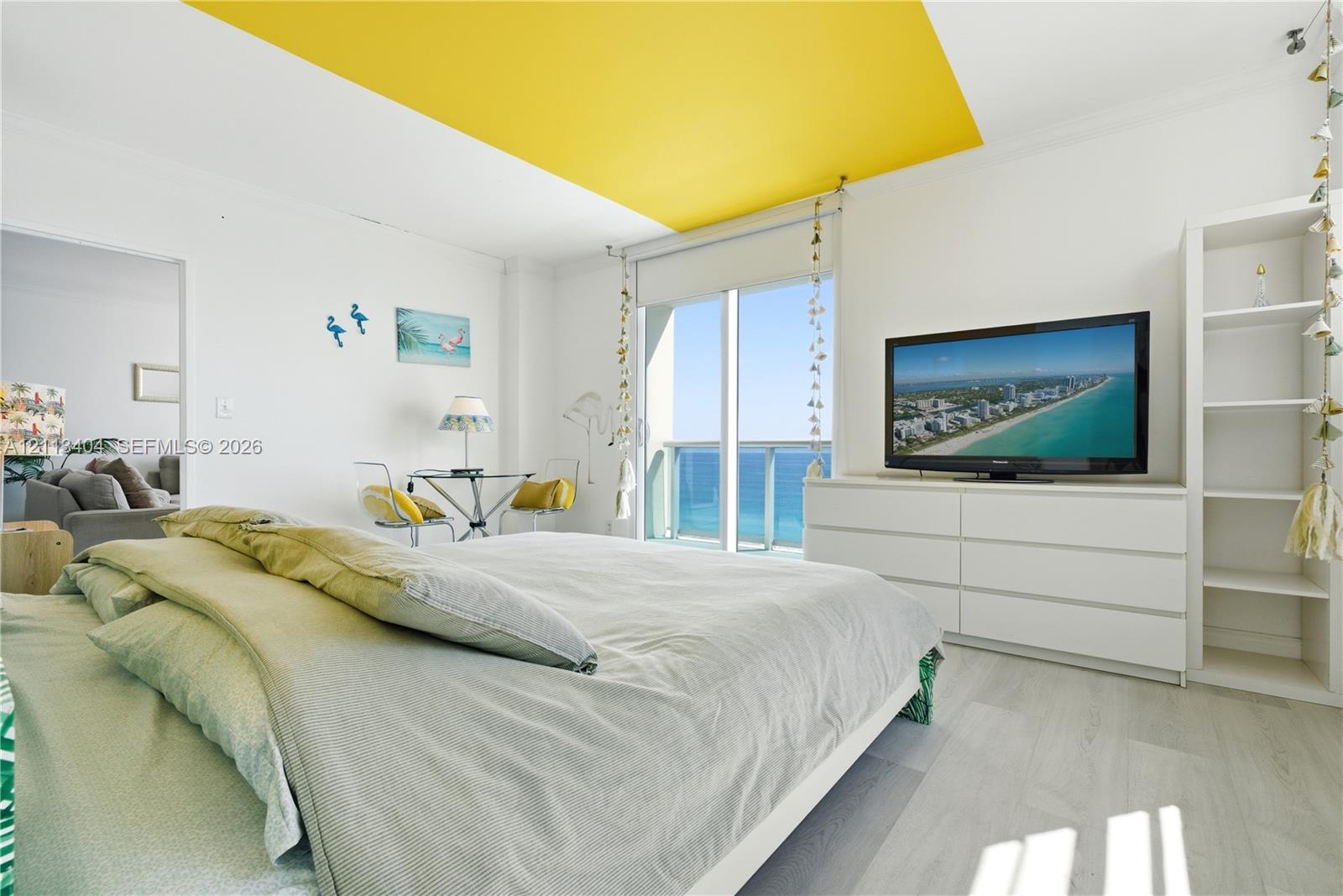 Full-height sliding glass doors with direct ocean access, integrated white built-in shelving, wood-finish flooring, and recessed ceiling feature