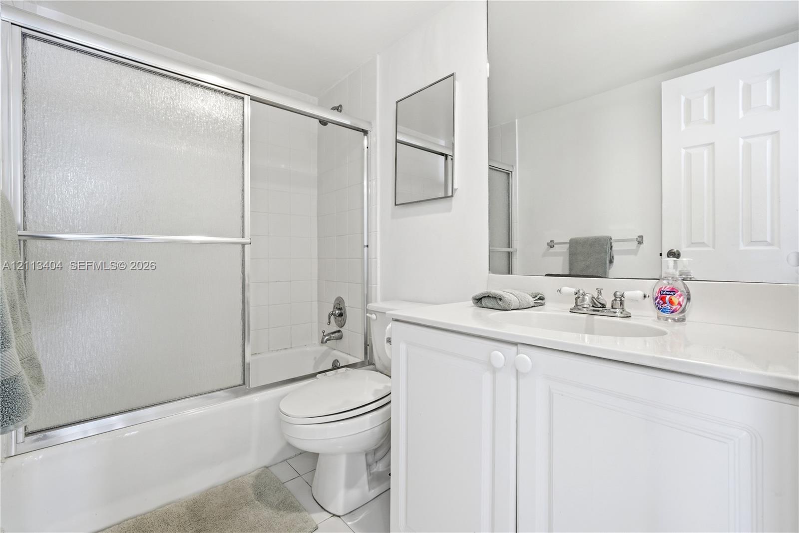Bathroom featuring a white vanity cabinet with a stone-top integrated sink, chrome dual-handle faucet, oversized wall-mounted mirror, and a shower-tub combination enclosed by sliding glass doors