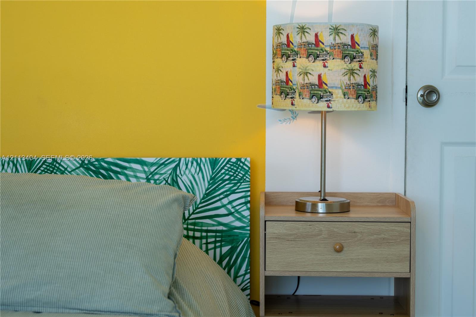 Multi-toned interior wall paint, wood-finish nightstand featuring a single storage drawer, and a classic six-panel door with a brushed nickel knob