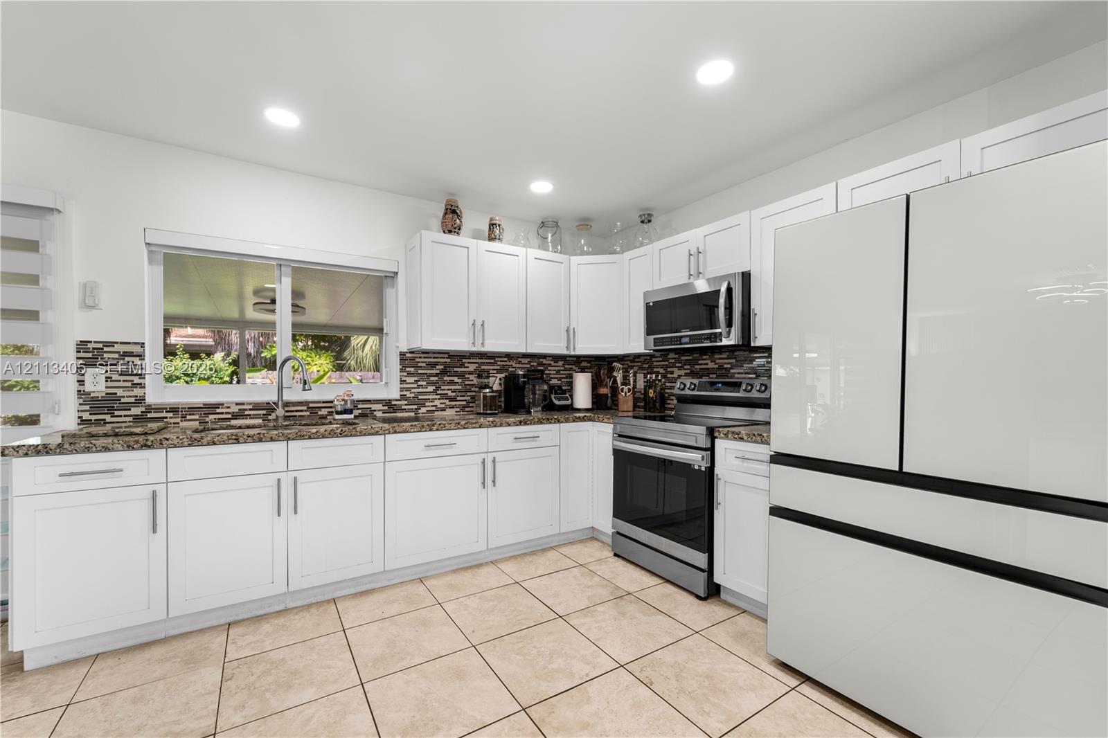 White shaker-style cabinetry, multi-tonal decorative tile backsplash, stone-finish countertops, stainless steel appliances, and ceramic tile flooring