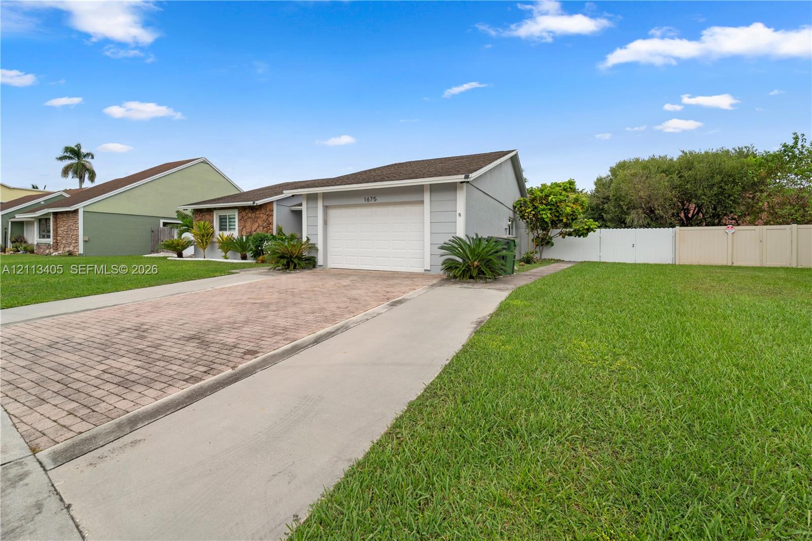 Single-story exterior featuring a paver driveway, an attached garage, and perimeter vinyl fencing