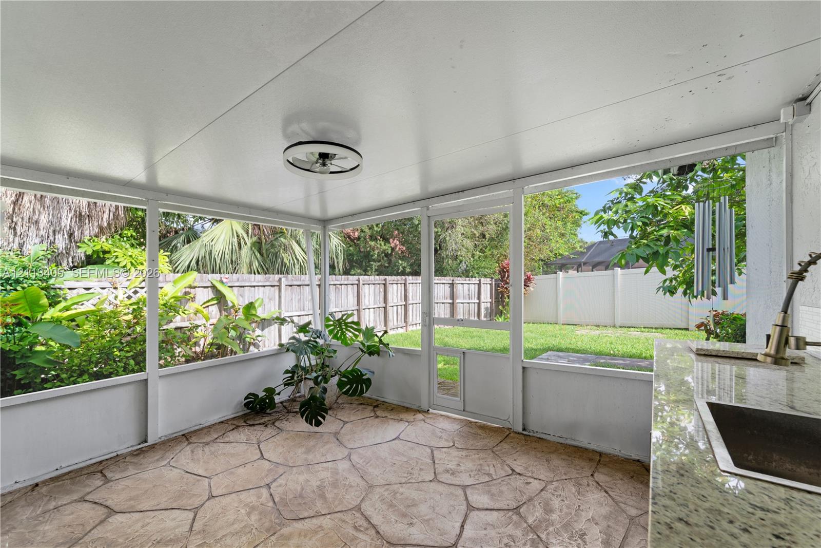 Screened patio featuring flagstone flooring, a built-in outdoor kitchen with a stone countertop, integrated sink, and ceiling-mounted light fixture