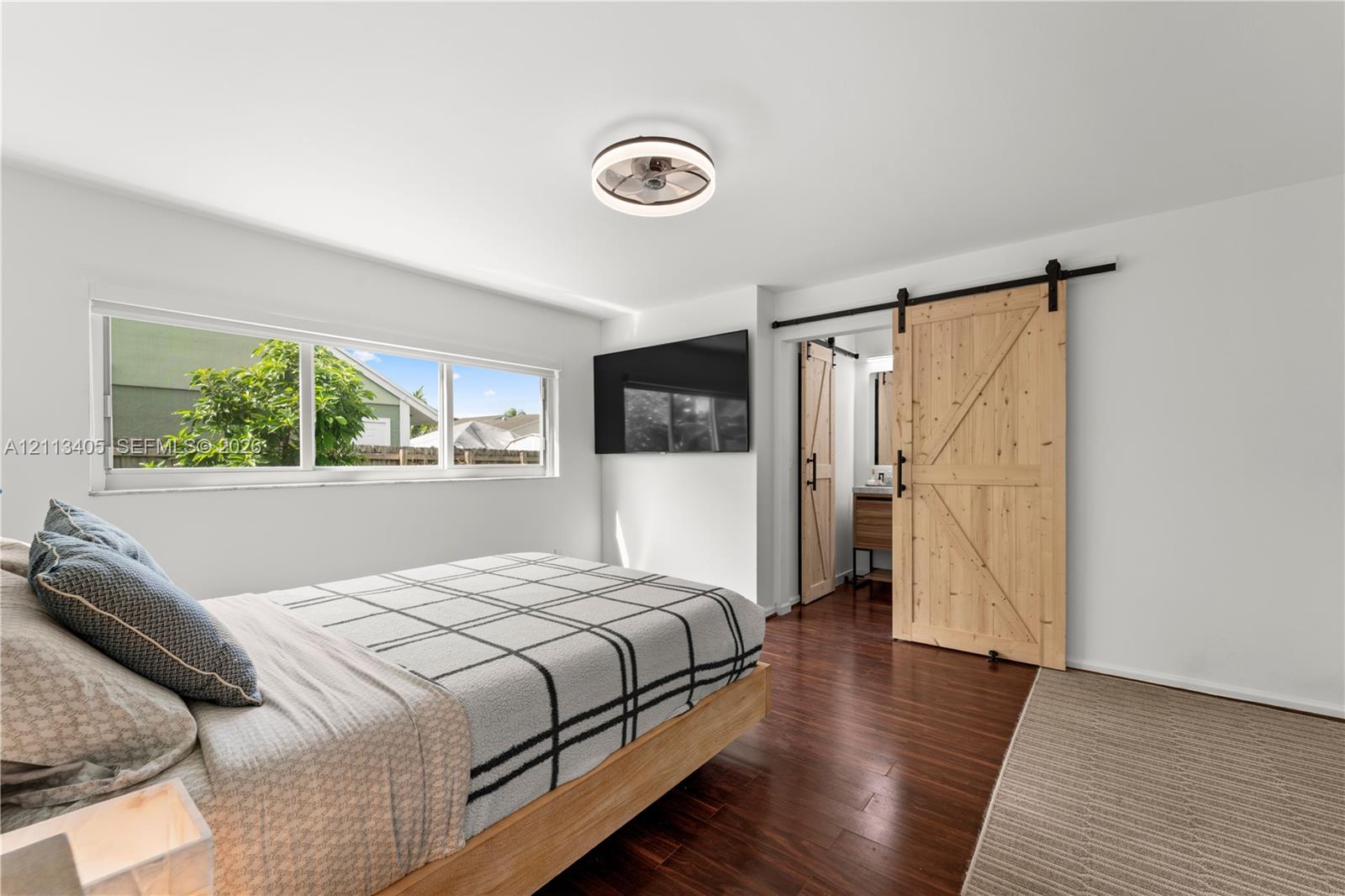 Wood-finish flooring, sliding wood barn door with matte black hardware, large picture window, and integrated circular ceiling fan with lighting