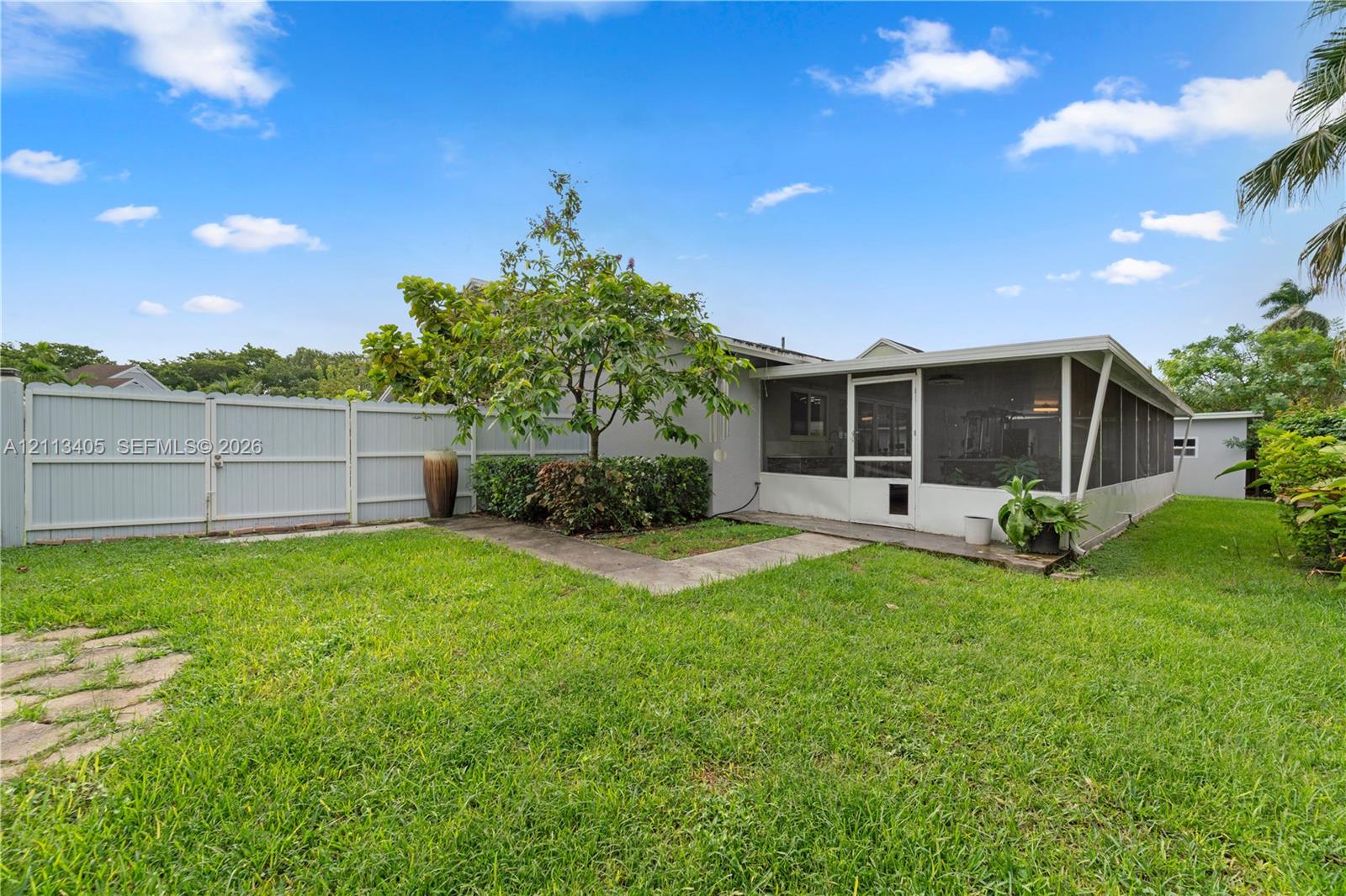 Backyard featuring a screened-in lanai, concrete walkway, and perimeter privacy fencing