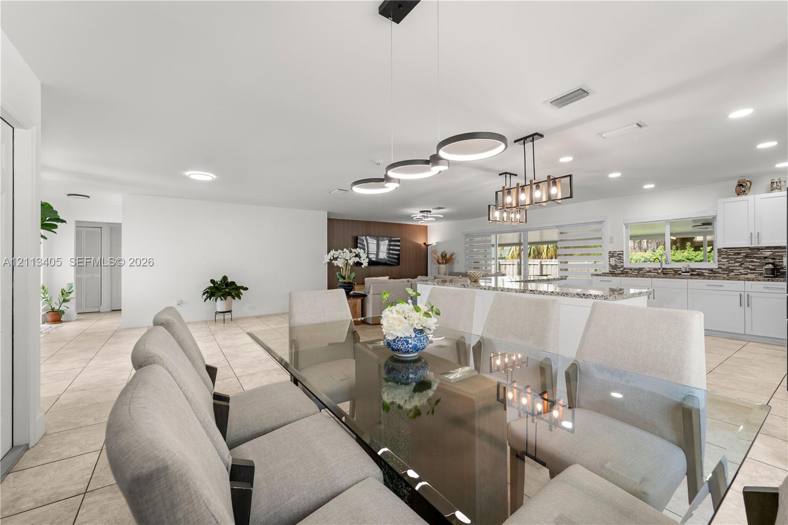 Open-concept living space featuring ceramic tile flooring, recessed lighting, modern geometric pendant chandeliers, white shaker-style cabinetry, and a stone-tiled backsplash