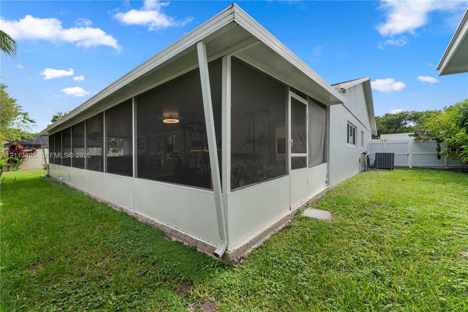 Enclosed screened-in patio featuring white aluminum framing, a solid roof structure, and a perimeter lawn