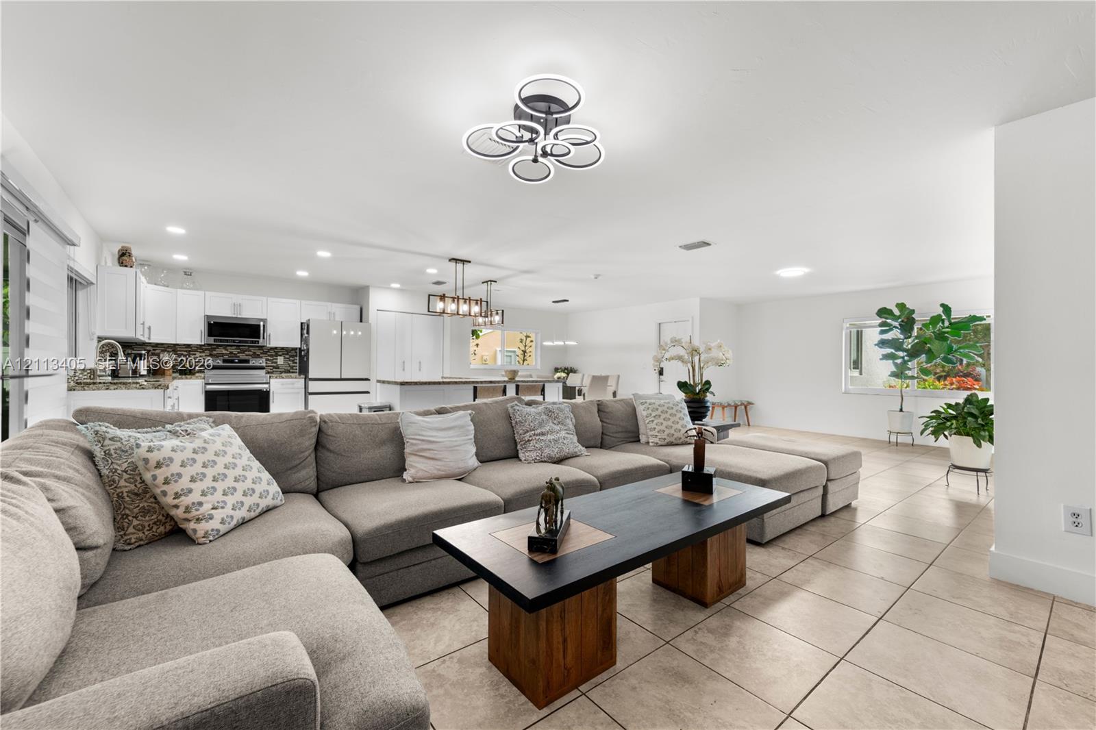 Open-concept living space featuring ceramic tile flooring, recessed lighting, modern geometric chandelier, and white cabinetry
