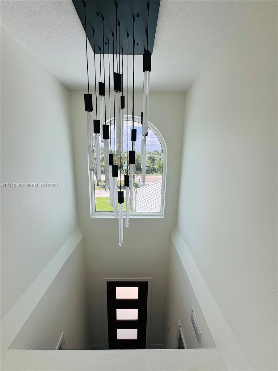 Multi-tiered contemporary chandelier featuring glass and black matte accents, complemented by an arched window and a modern entry door with three rectangular glass panels