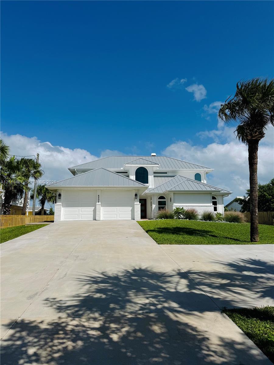 Two-story residence featuring a light-colored stucco exterior, a multi-gabled metal roof, arched window detailing, and an expansive concrete driveway Two-story residence featuring a light-colored stucco exterior, a multi-gabled metal roof, arched window detailing, and an expansive concrete driveway
