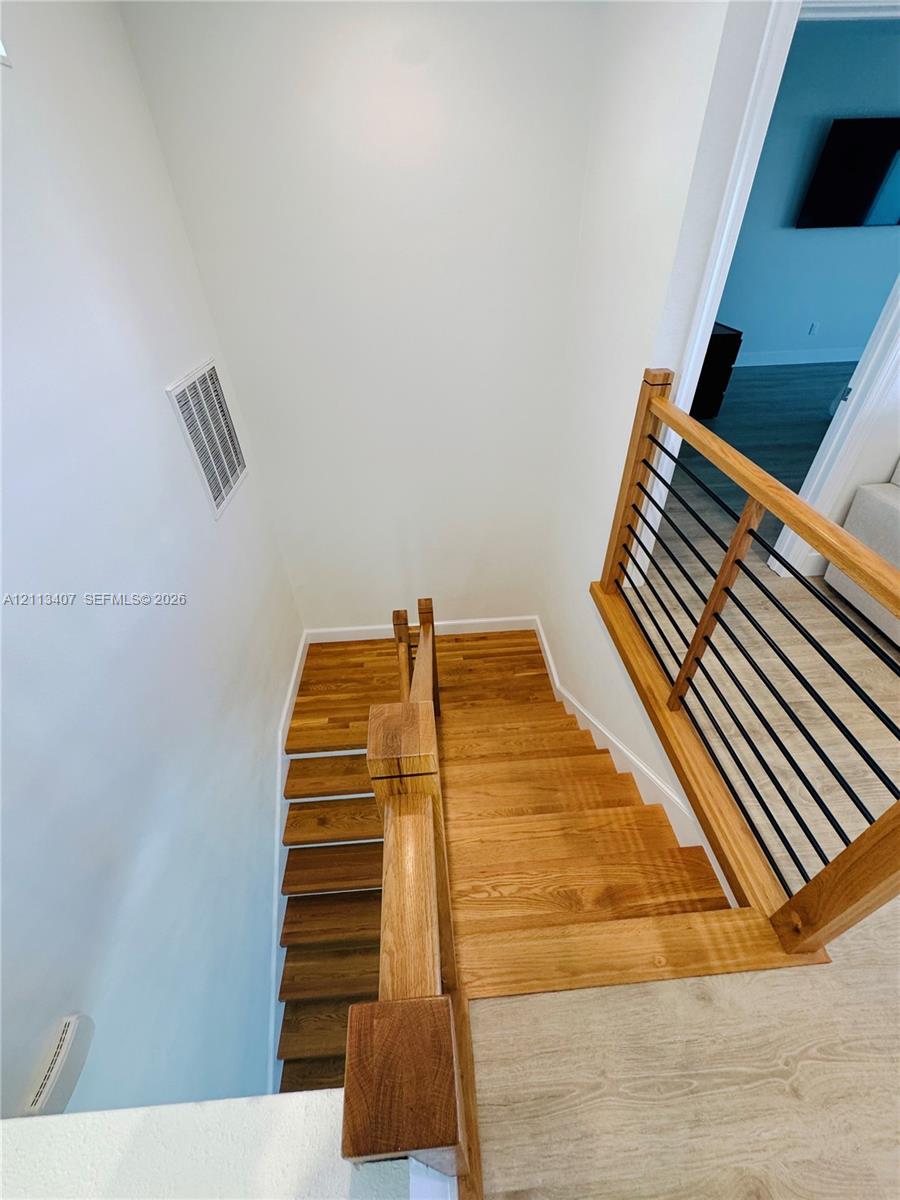 Staircase featuring wood-finish treads and a railing composed of wooden handrails with black metal balusters