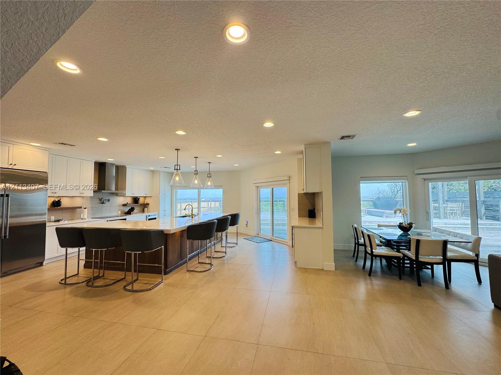 Open-concept interior featuring large-format tile flooring, recessed lighting, white cabinetry, a center island with a stone countertop, and glass sliding doors Open-concept interior featuring large-format tile flooring, recessed lighting, white cabinetry, a center island with a stone countertop, and glass sliding doors