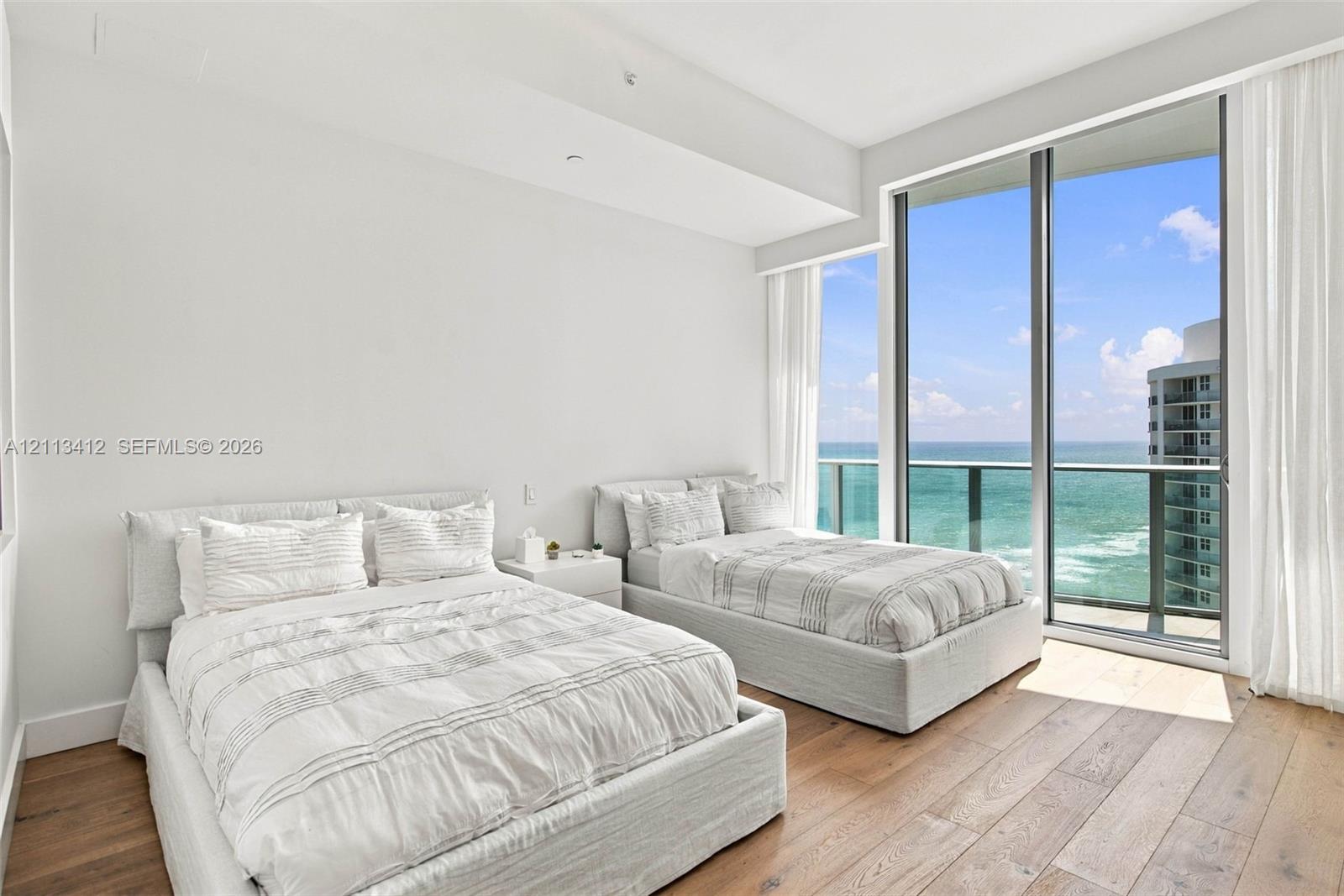 Floor-to-ceiling windows, wood-finish flooring, and direct ocean water backdrop