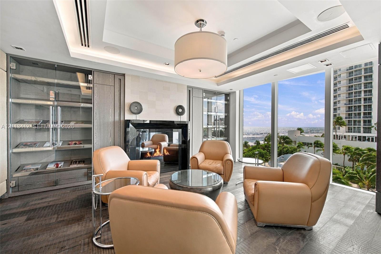 Floor-to-ceiling windows, wood-finish flooring, built-in display cabinetry, tray ceiling with recessed lighting, and a modern fireplace with a black glass surround