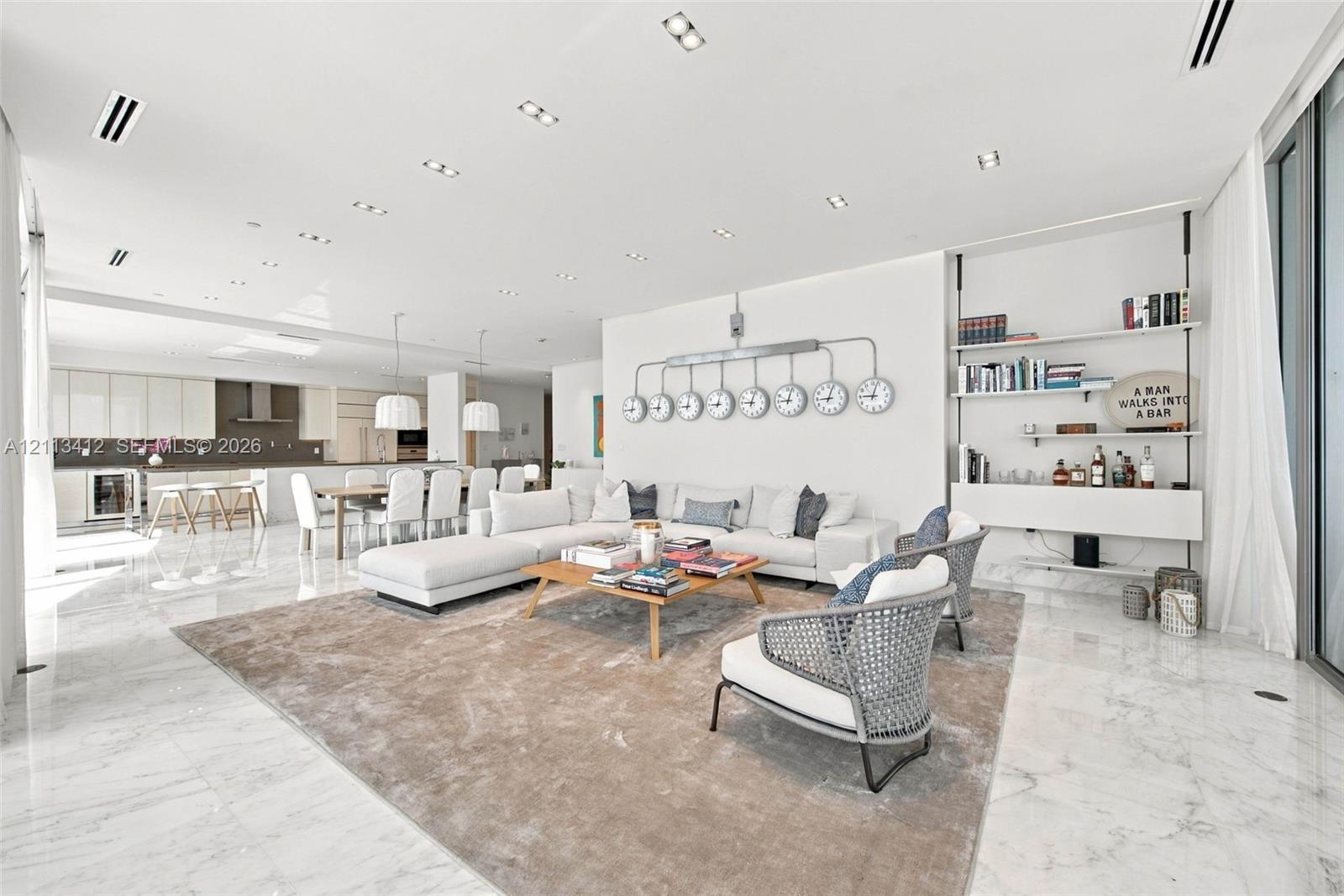 Open-concept interior featuring light-toned stone flooring, recessed ceiling lighting, and a wall-mounted shelving unit with integrated cabinetry Open-concept interior featuring light-toned stone flooring, recessed ceiling lighting, and a wall-mounted shelving unit with integrated cabinetry