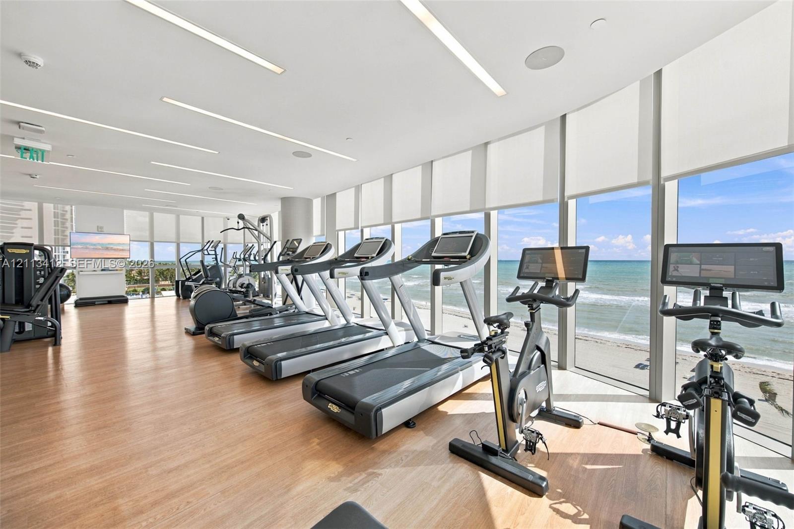 Fitness center featuring wood-finish flooring, floor-to-ceiling windows, and recessed linear lighting, with direct ocean backdrop
