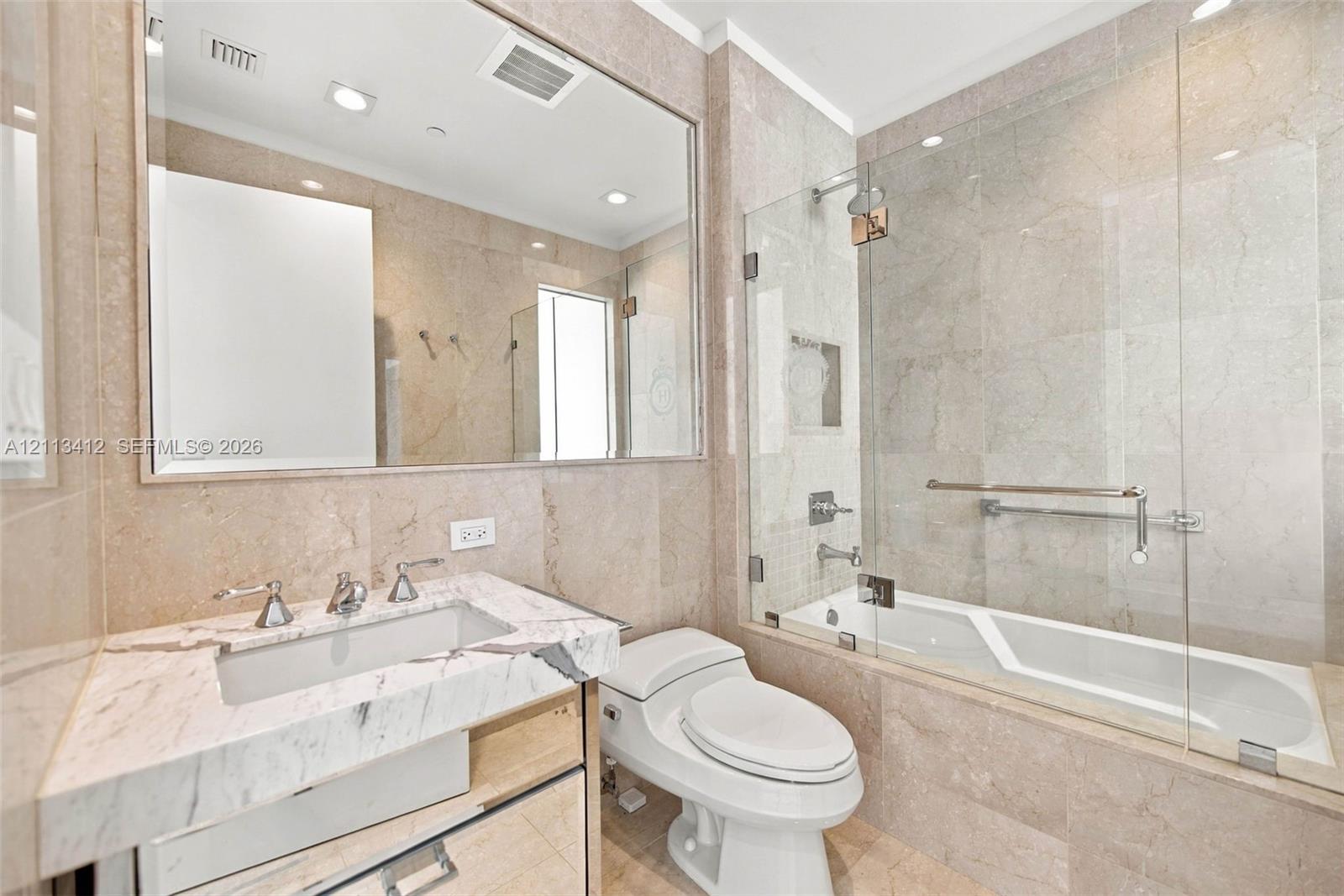 Full-height stone wall tiling, custom vanity with a stone countertop and undermount sink, frameless glass shower enclosure, and a large wall-mounted mirror