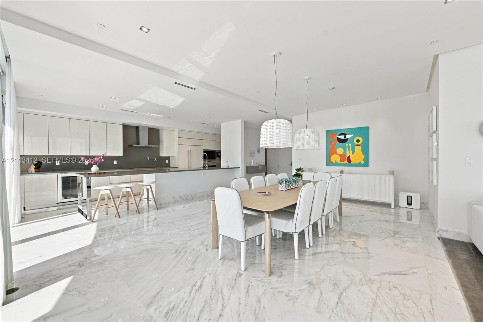 Open-concept kitchen and dining area featuring stone-finish flooring, high-gloss cabinetry, stainless steel range hood, built-in refrigerator, and dual pendant lighting fixtures Open-concept kitchen and dining area featuring stone-finish flooring, high-gloss cabinetry, stainless steel range hood, built-in refrigerator, and dual pendant lighting fixtures