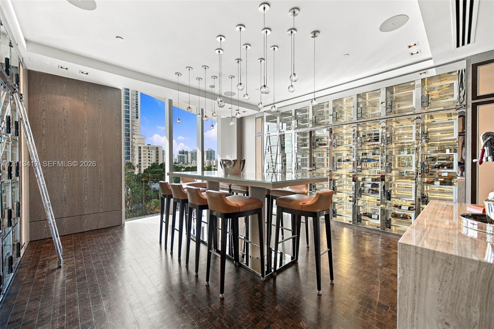 Custom temperature-controlled wine storage wall, floor-to-ceiling glass windows, wood-finish flooring, central island with quartz countertop, and multi-pendant lighting