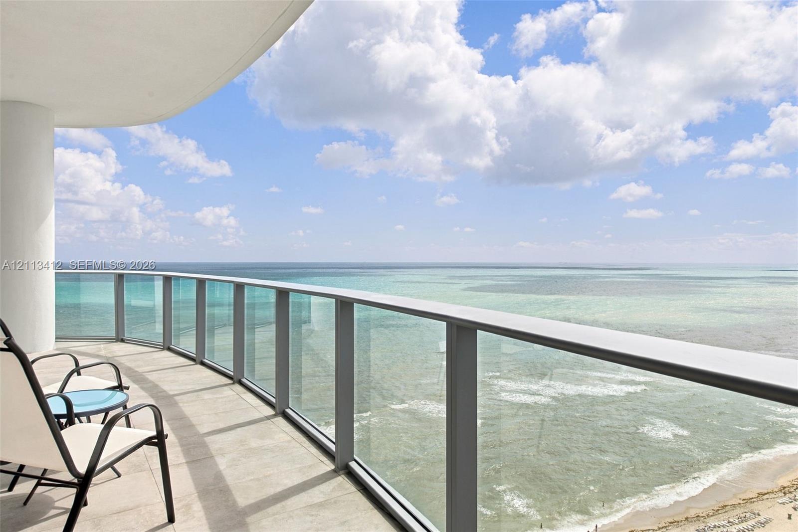Curved balcony featuring neutral stone-finish flooring and a glass-paneled railing Curved balcony featuring neutral stone-finish flooring and a glass-paneled railing