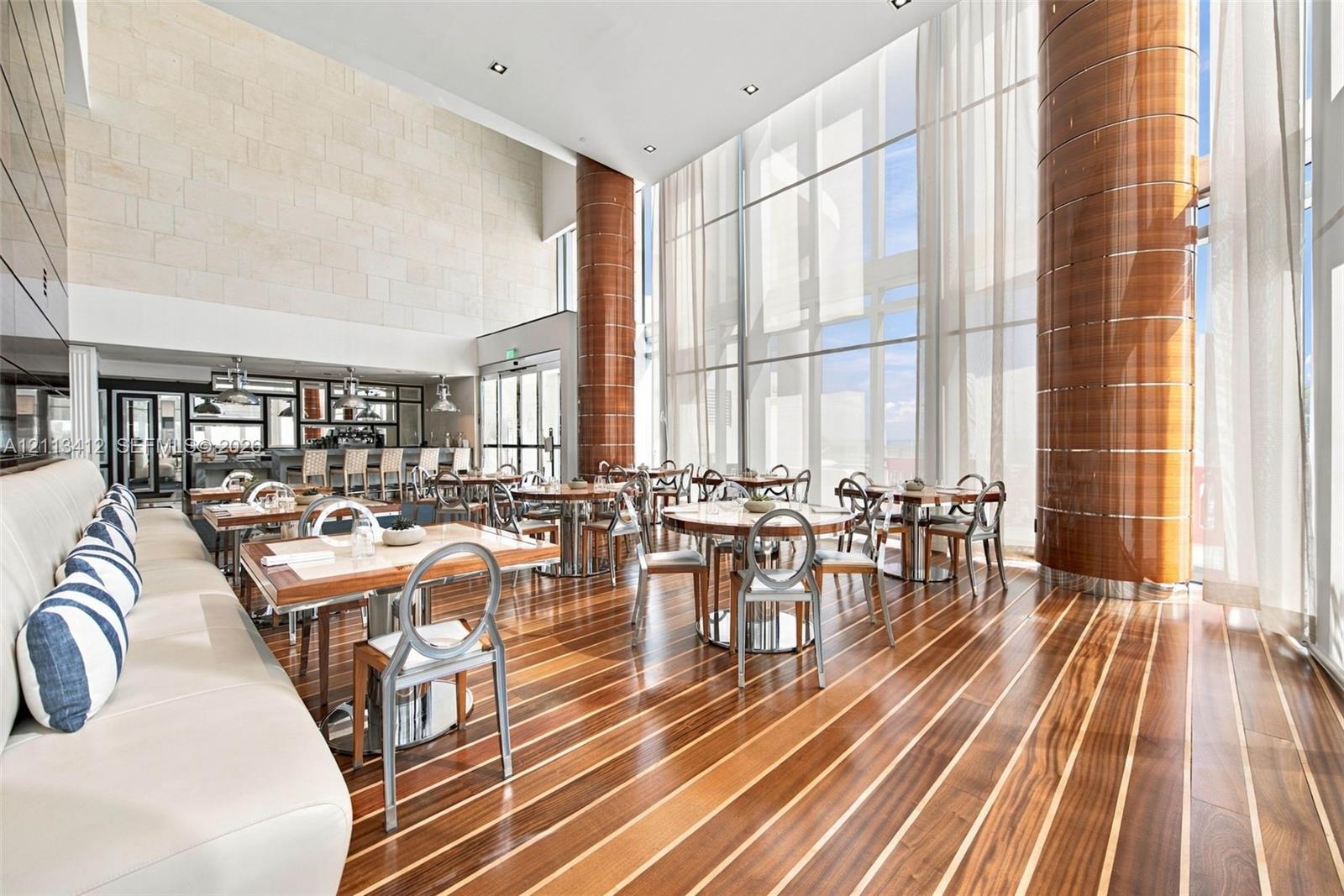 Double-height space featuring floor-to-ceiling glass, inlaid wood-finish flooring, decorative cylindrical columns with wood-toned cladding, and textured stone accent wall