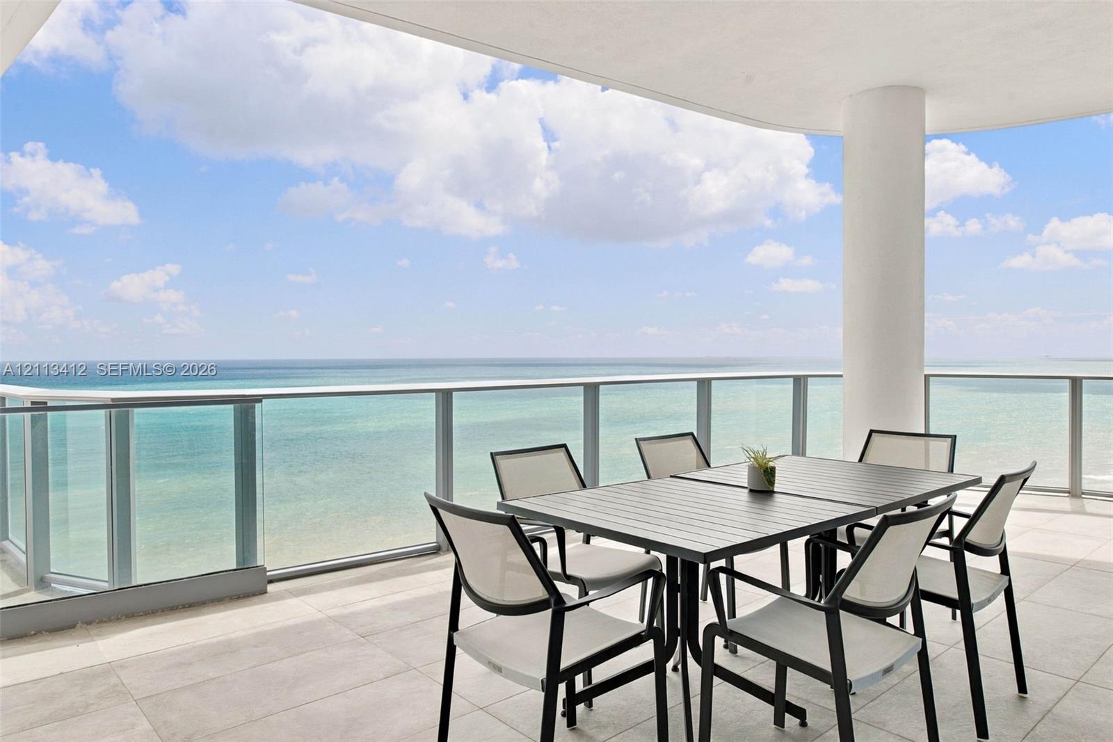 Covered balcony featuring oversized stone-style tile flooring, glass panel railings, and a structural support column Covered balcony featuring oversized stone-style tile flooring, glass panel railings, and a structural support column